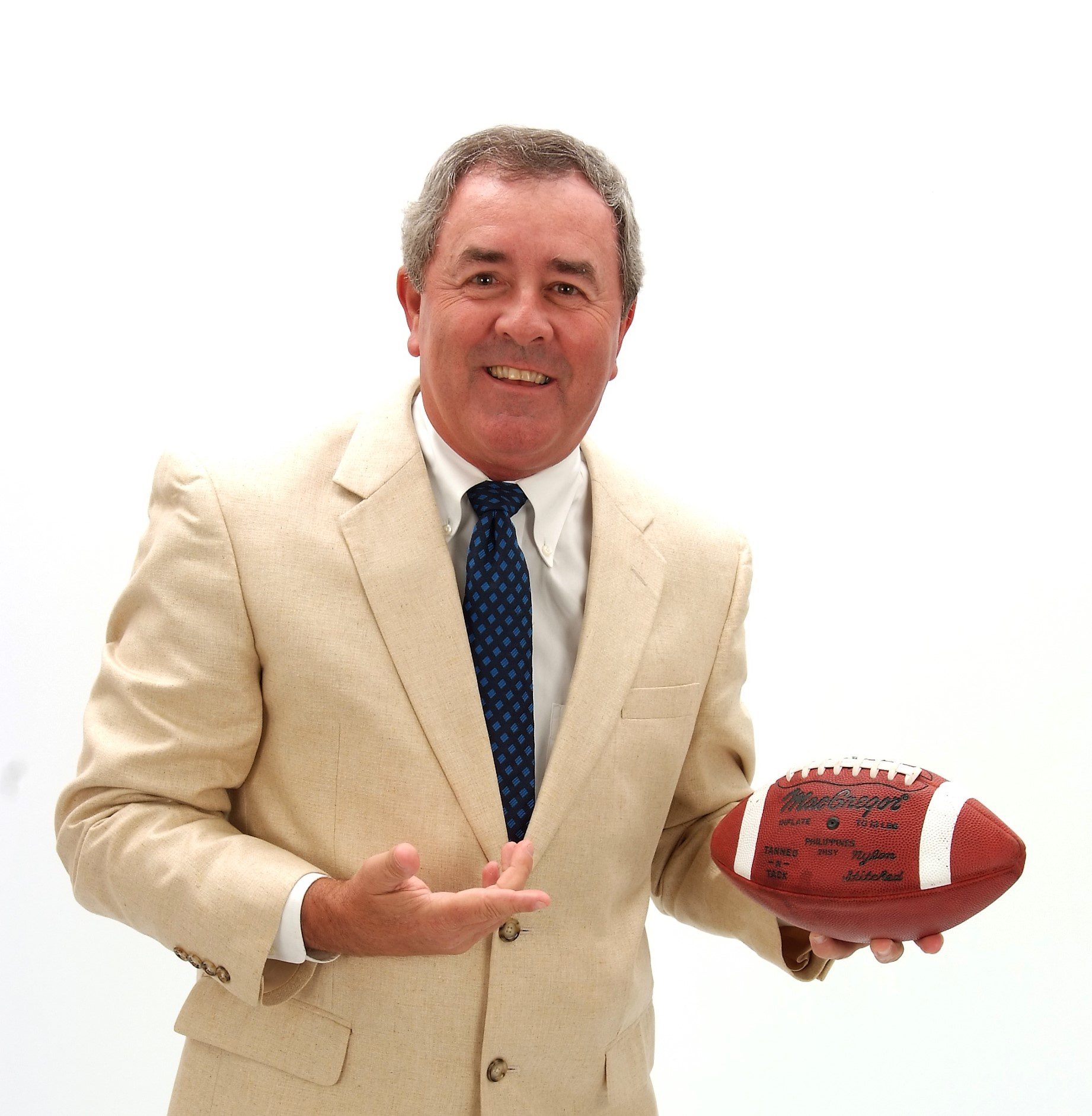 Smiling man in beige suit holding a football.