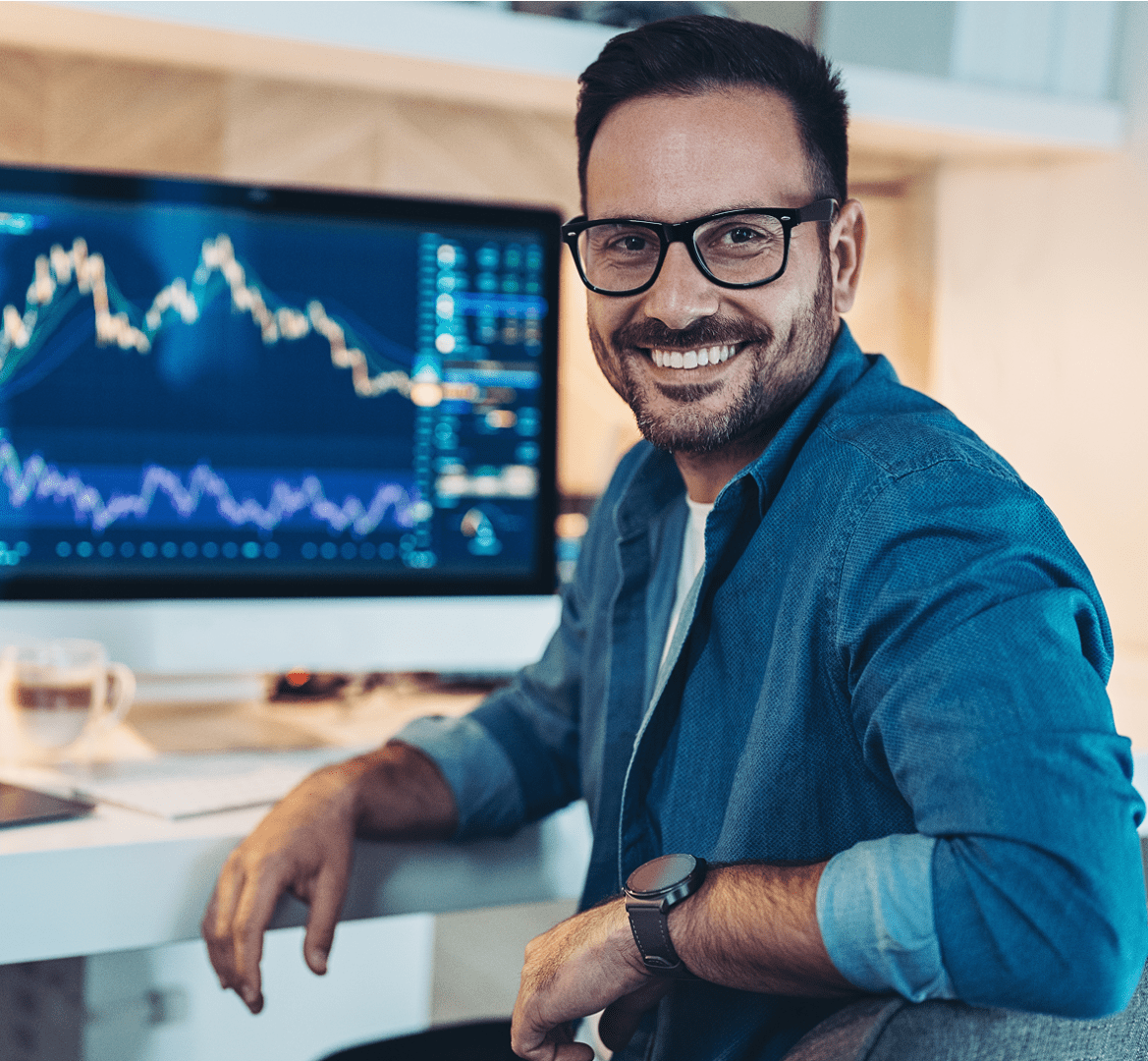 Man smiling at desk with stock charts