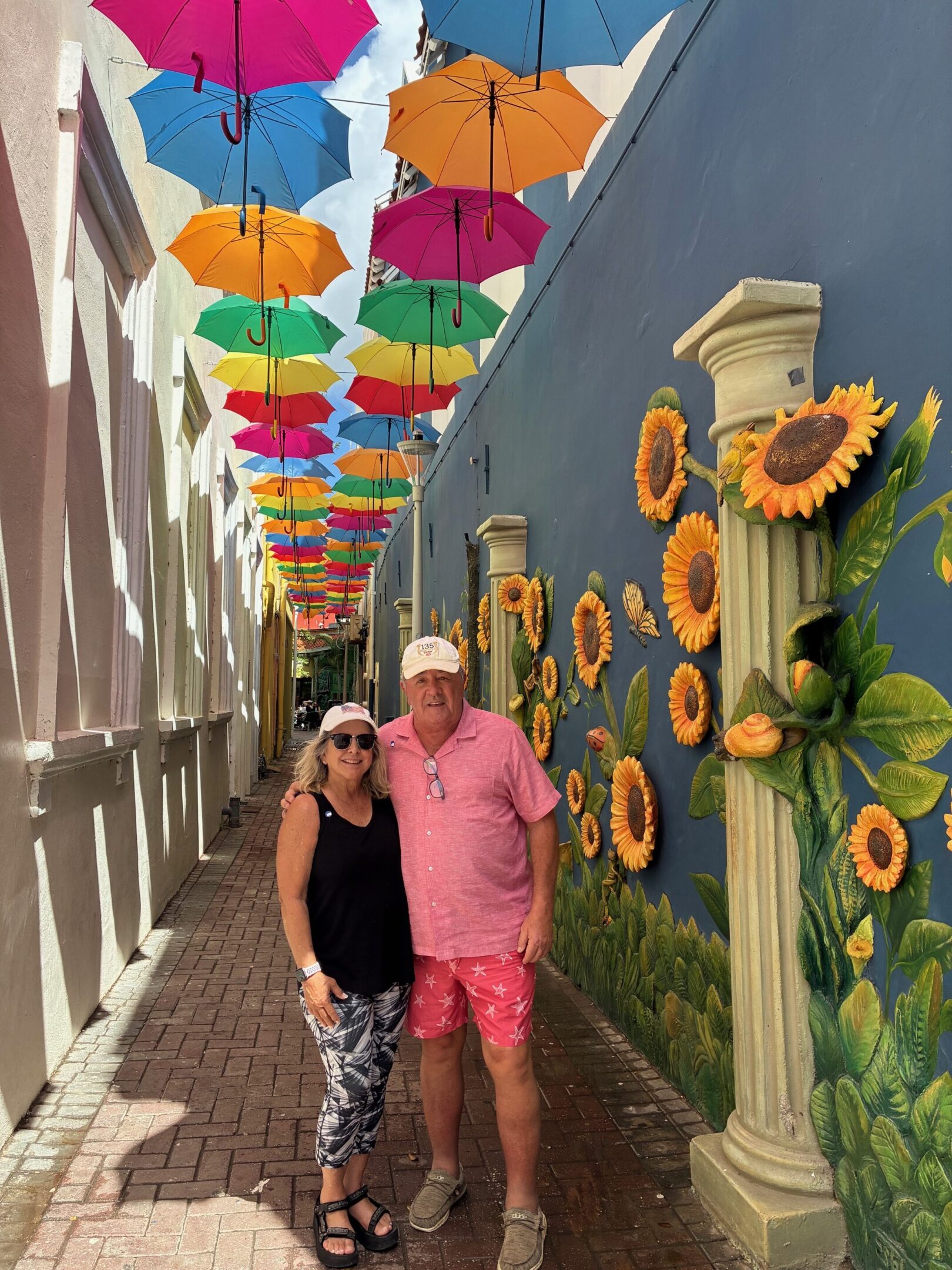 A couple posing under colorful umbrellas and sunflower decorations.